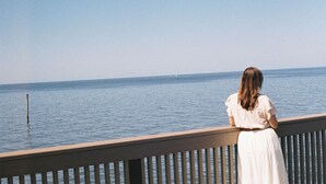 A person sitting on a wooden railing overlooking a calm body of water. - The Fairhope Bay Room (Fairhope)