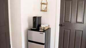 A compact kitchenette with a coffee maker, a basket with cups, and a hanging lantern. - The Fairhope Bay Room (Fairhope)