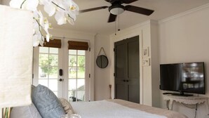 A bedroom with a bed, a ceiling fan, a TV on a small table, and a door leading to a balcony. - The Fairhope Bay Room (Fairhope)
