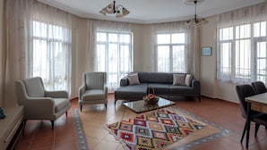 Ein geräumiges Wohnzimmer mit grauem Sofa, zwei Sesseln, einem Couchtisch und einem farbenfrohen Teppich.