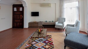 Ein Wohnzimmer mit Fernseher, zwei Sesseln, einem gemusterten Teppich und einem Deckenventilator.