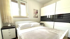 A bedroom with a bed, bedside tables, a nightstand, a window with curtains, and a wall-mounted wardrobe. - Apartment Maria close to the beach and city center (Umag)