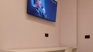 Ein modernes Zimmer mit einem weißen Schreibtisch, einem Stuhl und einem an der Wand befestigten Flachbildfernseher.