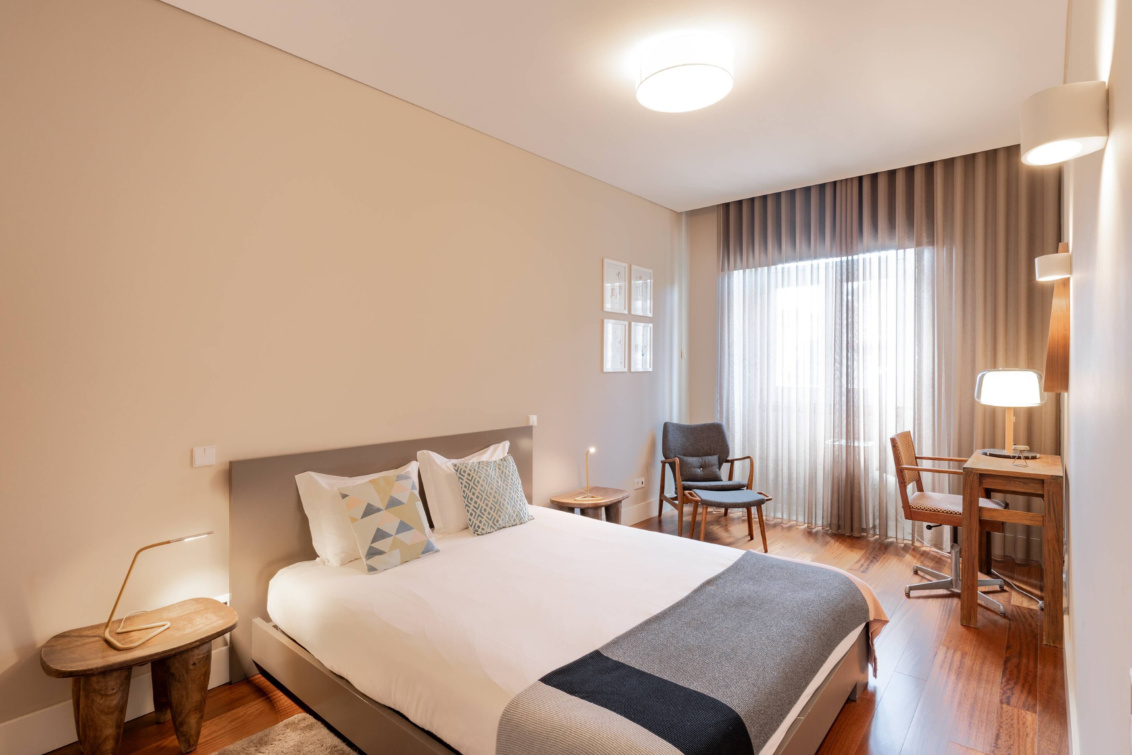 A hotel room with a large bed, a desk, a chair, and a lamp.