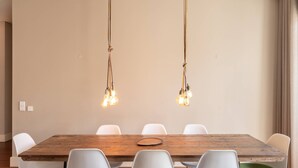 A dining area with a wooden table and white chairs, two hanging light fixtures, and a beige wall. - VIVA Aliados Spacious & Bright Flat (Porto)