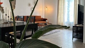 A modern living room with a dining area, featuring a sofa, TV, and large green plants. - Appartement Spacieux et Calme (Bussy-Saint-Georges)