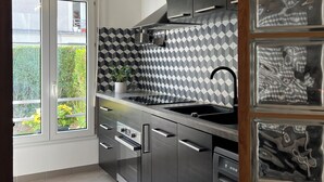 A modern kitchen with a geometric backsplash, stainless steel appliances, and a window with a view of greenery. - Appartement Spacieux et Calme (Bussy-Saint-Georges)