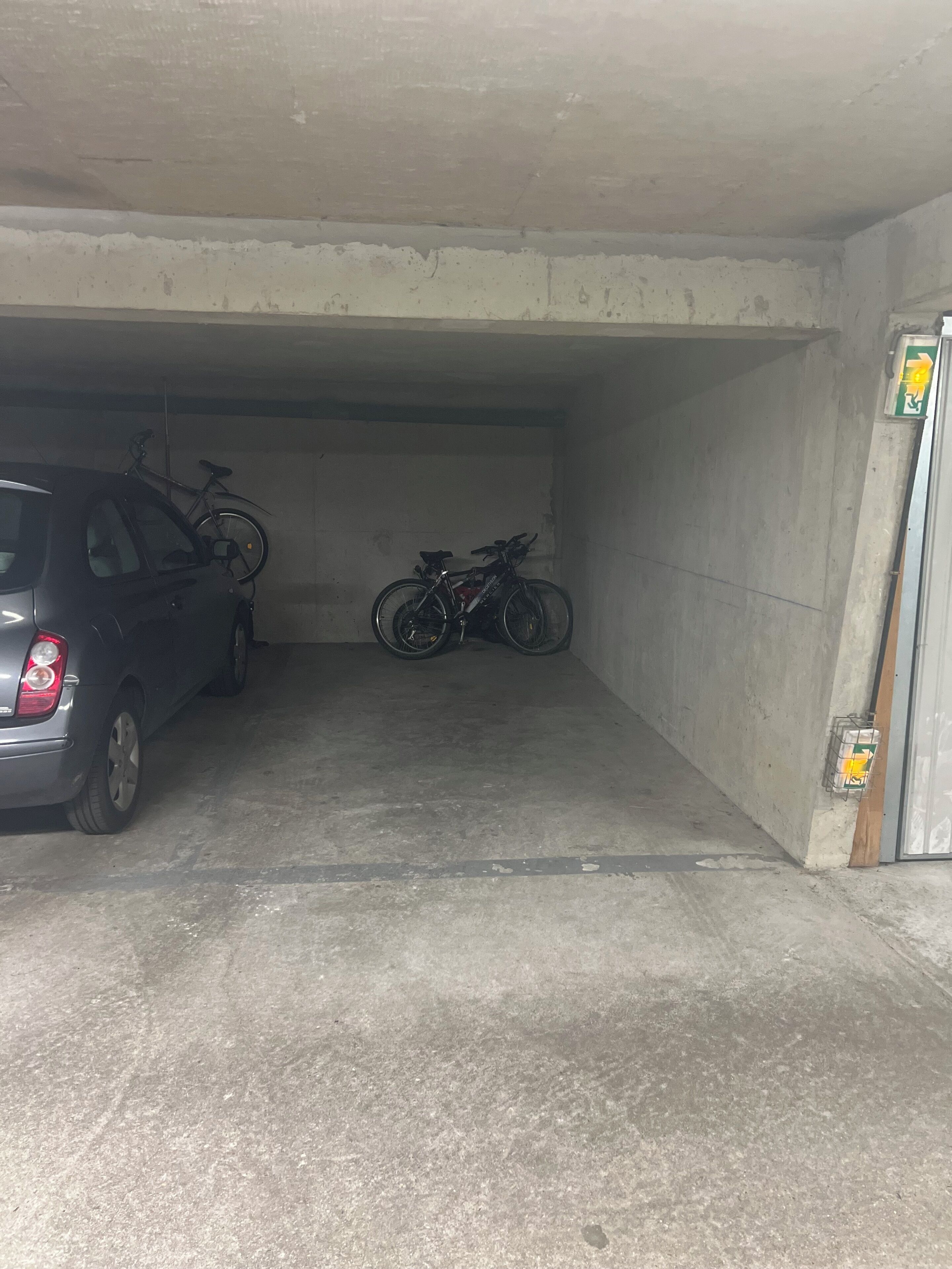 A parking garage with a car and two bicycles parked inside.