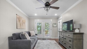 Un salon avec un canapé gris, un meuble en bois, un téléviseur et un ventilateur de plafond.