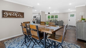Un coin repas avec une table et des chaises en bois, une cuisine à l’arrière-plan et un panneau indiquant « rassemblement » sur le mur.