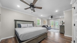 Une chambre dotée d’un grand lit, d’un plancher en bois, d’un ventilateur de plafond et offrant une vue sur l’extérieur.