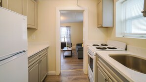 A kitchen with a refrigerator, stove, and sink. There is a dining area with a table and chairs in the background. - Renovated One Bedroom Apartment Downtown Falmouth Minutes From the Beach  (Falmouth)