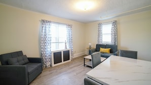 A modern living room with a grey sofa, a dining table, and patterned curtains. - Renovated One Bedroom Apartment Downtown Falmouth Minutes From the Beach  (Falmouth)