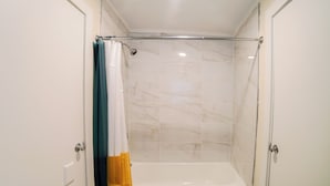 A shower with a glass door, a white bathtub, and a curtain. - Renovated One Bedroom Apartment Downtown Falmouth Minutes From the Beach  (Falmouth)