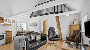 A spacious living area with a black leather sofa, a wooden coffee table, and a black armchair. A staircase with a black railing leads to an upper level.