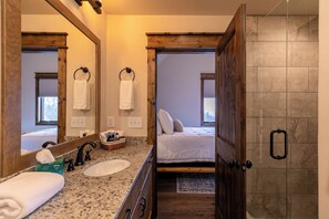 A bathroom with a large mirror, a sink, and a shower. There is a bed visible through the door. - Timberline at Eagles Nest (Banner Elk)