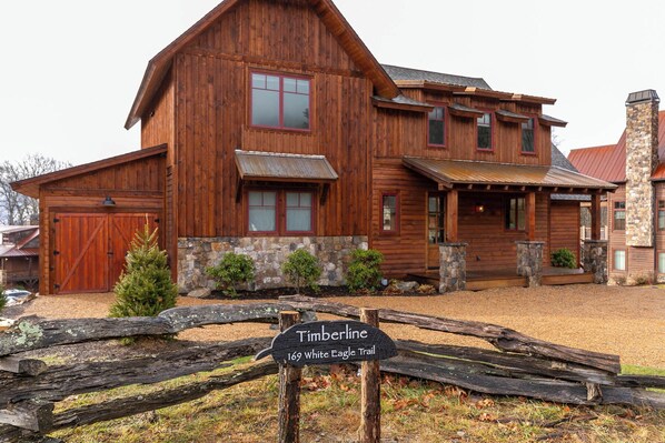 A large wooden cabin with a stone foundation, a covered porch, and a sign indicating it is located on the 169 White Eagle Trail. - Timberline at Eagles Nest (Banner Elk)