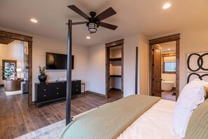 A bedroom with a bed, a ceiling fan, a dresser, a TV, and a bathroom visible through an open door. - Timberline at Eagles Nest (Banner Elk)