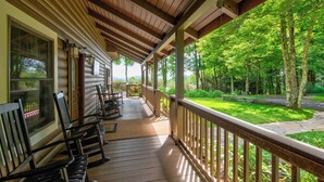 A covered porch with wooden railings, rocking chairs, and a view of a green landscape with trees. - Mountaintop at Yonahlossee Saddle (Boone)