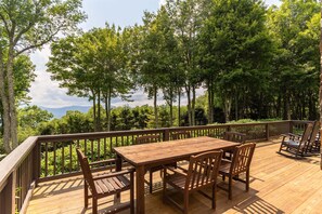 A wooden deck with a table and chairs, surrounded by trees and a view of the mountains. - Mountaintop at Yonahlossee Saddle (Boone)