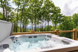 Ein Whirlpool mit Holzterrasse und Blick auf ein bewaldetes Gebiet.