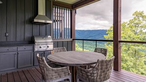A covered outdoor kitchen with a grill, dining table, and wicker chairs. - Camp Cotter at Blue Ridge Mountain (Lenoir)