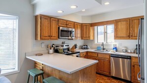 A modern kitchen with wooden cabinets, stainless steel appliances, and a large island with bar stools. - Chetola: Chestnut 8 (Blowing Rock)