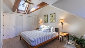 A bedroom with a sloped ceiling, a bed with striped bedding, two wall-mounted lamps, a nightstand, a potted plant, and a skylight. - Chetola: Chestnut 8 (Blowing Rock)