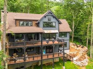A multi-story cabin with a deck, large windows, and a stone foundation. - Knotty by Nature at Eagles Nest (Banner Elk)