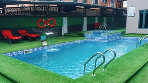 A swimming pool with artificial grass, red lounge chairs, and a lifebuoy. - Rolarz Resorts & Hotel (Benin City)