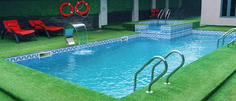 A swimming pool with artificial grass, red lounge chairs, and a lifebuoy.