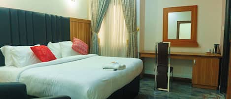 A hotel room with a bed, a desk, a chair, a mirror, and an air conditioning unit.