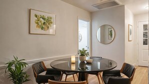 Een eethoek met een ronde tafel, vier stoelen, een potplant en kunstwerken in lijsten aan de muren.