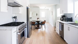 Een moderne keuken met witte kastjes, roestvrijstalen apparatuur en een eethoek met een ronde tafel en stoelen.