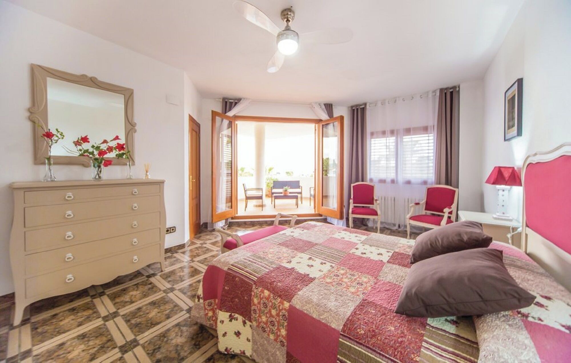 A bedroom with a bed, dresser, mirror, and a balcony with chairs.