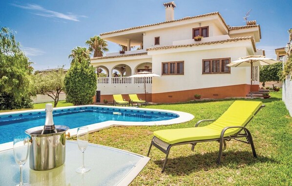 Een tweelaags huis met een zwembad, een terras met lounge stoelen en een tafel met champagnekoeler en glas.