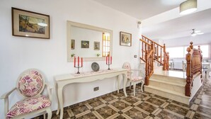 A hallway with a marble floor, a wooden staircase, and a console table with a mirror and framed pictures.