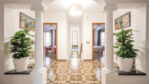 A hallway with a checkered floor, white columns, and potted plants on either side.