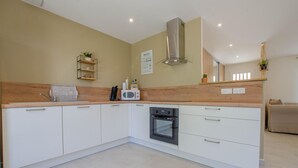 A modern kitchen with white cabinets, a stainless steel range hood, a microwave, and an oven. There is a wooden countertop and a small shelf with a plant. - Au jardin d'Olga - MESNIL SAINT PERE (MESNIL SAINT PERE)
