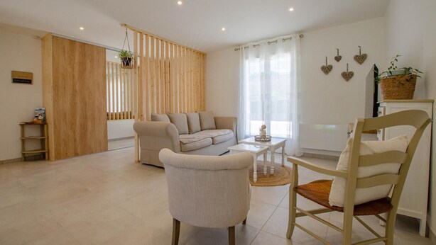 A modern living room with a sofa, a coffee table, and a chair. There is a wooden partition with a plant, and a wall with heart-shaped decorations. - Au jardin d'Olga - MESNIL SAINT PERE (MESNIL SAINT PERE)