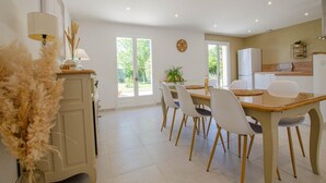 A modern kitchen with white cabinets, a wooden dining table with chairs, and a large window providing natural light. - Au jardin d'Olga - MESNIL SAINT PERE (MESNIL SAINT PERE)