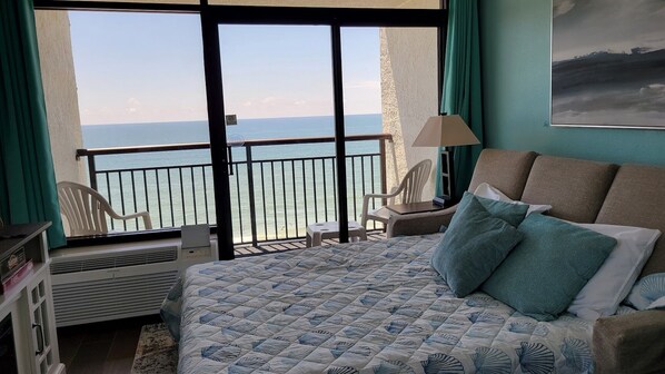 Un dormitorio con cama, una silla, un escritorio y vista al mar.