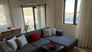 A living room with a grey sectional sofa, a small table with a red bowl, and a view of the outdoors through large windows. - 2 Bedroom sea view Kalkan in the center - Cactus (Antalya)