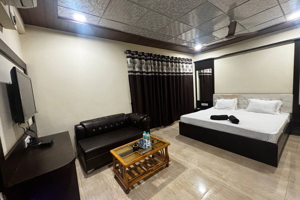 A hotel room with a bed, a sofa, a coffee table, a TV, and curtains.