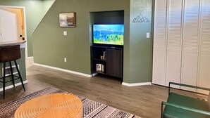 A living room with a TV, a bookshelf, a chair, and a patterned rug. - 2BR Historic Downtown Townhouse. Near Mt. Rainier, Waterfalls & Wildlife (Eatonville)