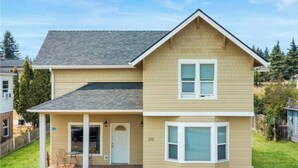 A two-story house with a front porch, a garage, and a number '210' on the side. - 2BR Historic Downtown Townhouse. Near Mt. Rainier, Waterfalls & Wildlife (Eatonville)