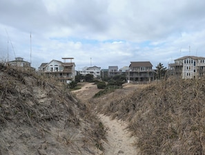 Zona residencial costera con varias casas de dos pisos, con balcones y un sendero arenoso que atraviesa el paisaje.