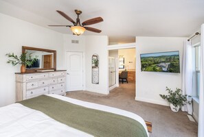 Ein Schlafzimmer mit Bett, Schminktisch, Deckenventilator und einem Landschaftsbild.