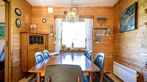 A wooden-paneled dining room with a large table and chairs, a chandelier, and a window with curtains. - Cottage with spectacular views (Ballangen)