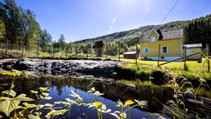 A yellow house with a metal roof, surrounded by a fence and a small pond with water lilies. - Cottage with spectacular views (Ballangen)